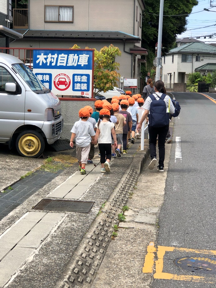 子どもたちの列と保育士さんが歩道を歩いているところの写真です。