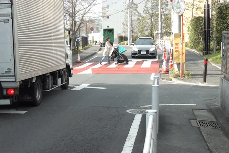 乳母車を押した女性がスムーズ横断歩道を渡るところの写真です。トラックと乗用車が停まって待っています。