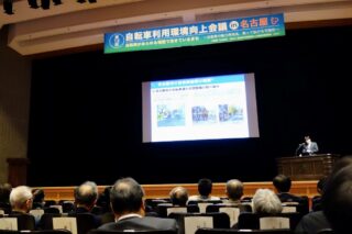 講演会場の様子。壇上の発表者と大勢の出席者。