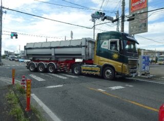 交差点で大きなダンプカーが右折しているところの写真です。