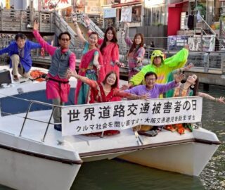 道頓堀に浮かぶ小船の上でダンサーと会員たちがポーズを取っているところの写真です。